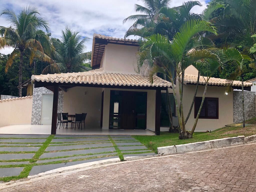 A two-story house with a tiled roof, a covered patio with chairs, and a paved driveway.