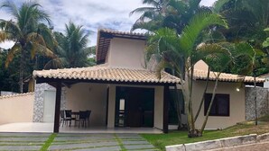 A two-story house with a tiled roof, a covered patio with chairs, and a paved driveway.