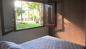 A bedroom with a bed, a window, and a view of a garden.