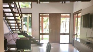 A spacious living area with a staircase, a dining table with chairs, and a television mounted on the wall.