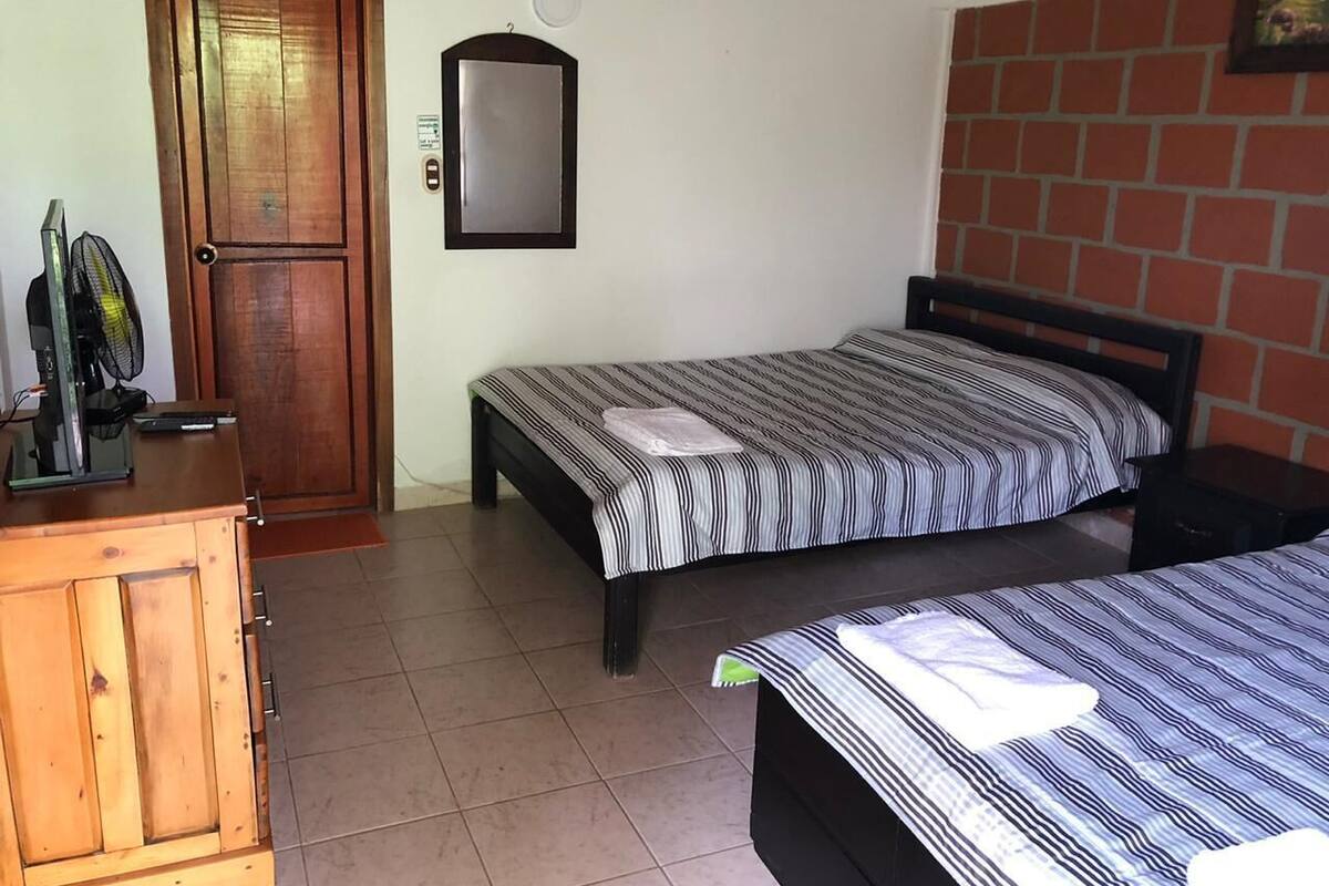 A room with two beds, a wooden cabinet, a door, and a wall-mounted mirror.