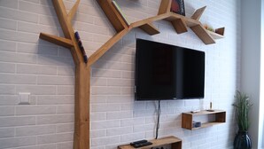 A modern living room with a flat-screen TV mounted on a white brick wall, wooden shelves, and a plant. - -30% off  Natalité Houzz Tbilisi (Tbilisi)