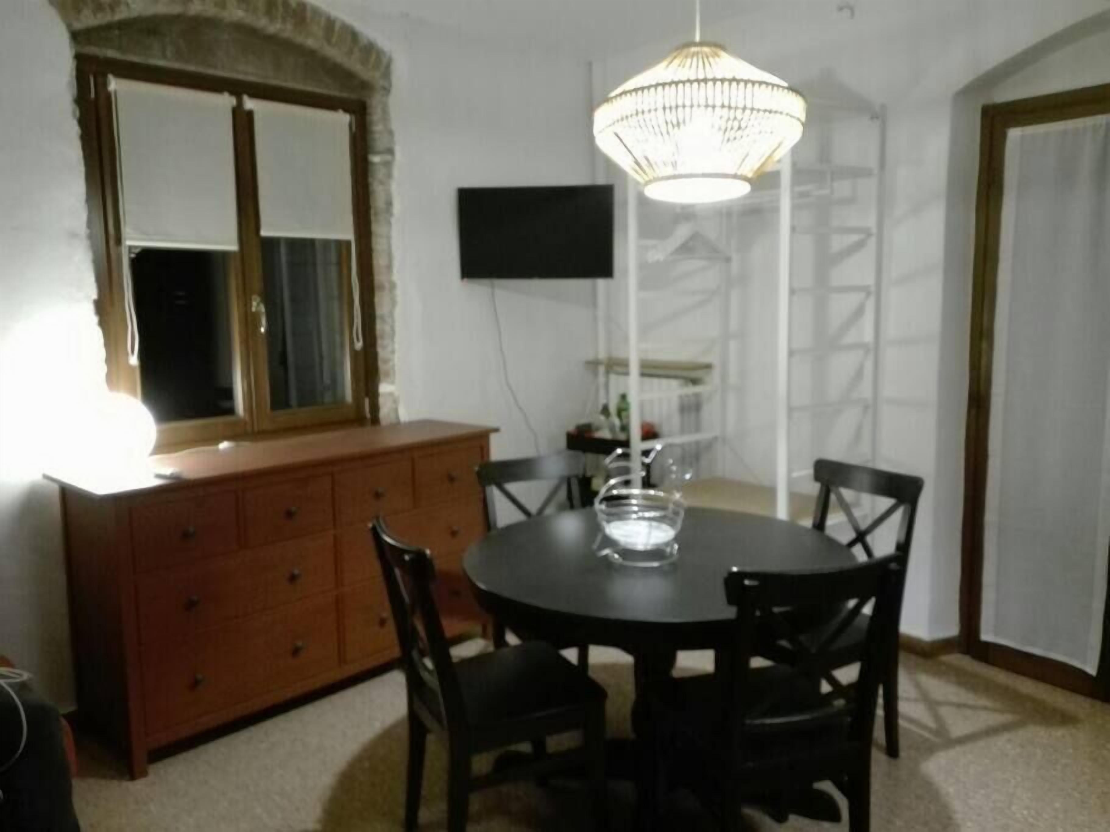 Un coin repas comprenant une table ronde, quatre chaises, un buffet en bois, un téléviseur fixé au mur et un luminaire suspendu.