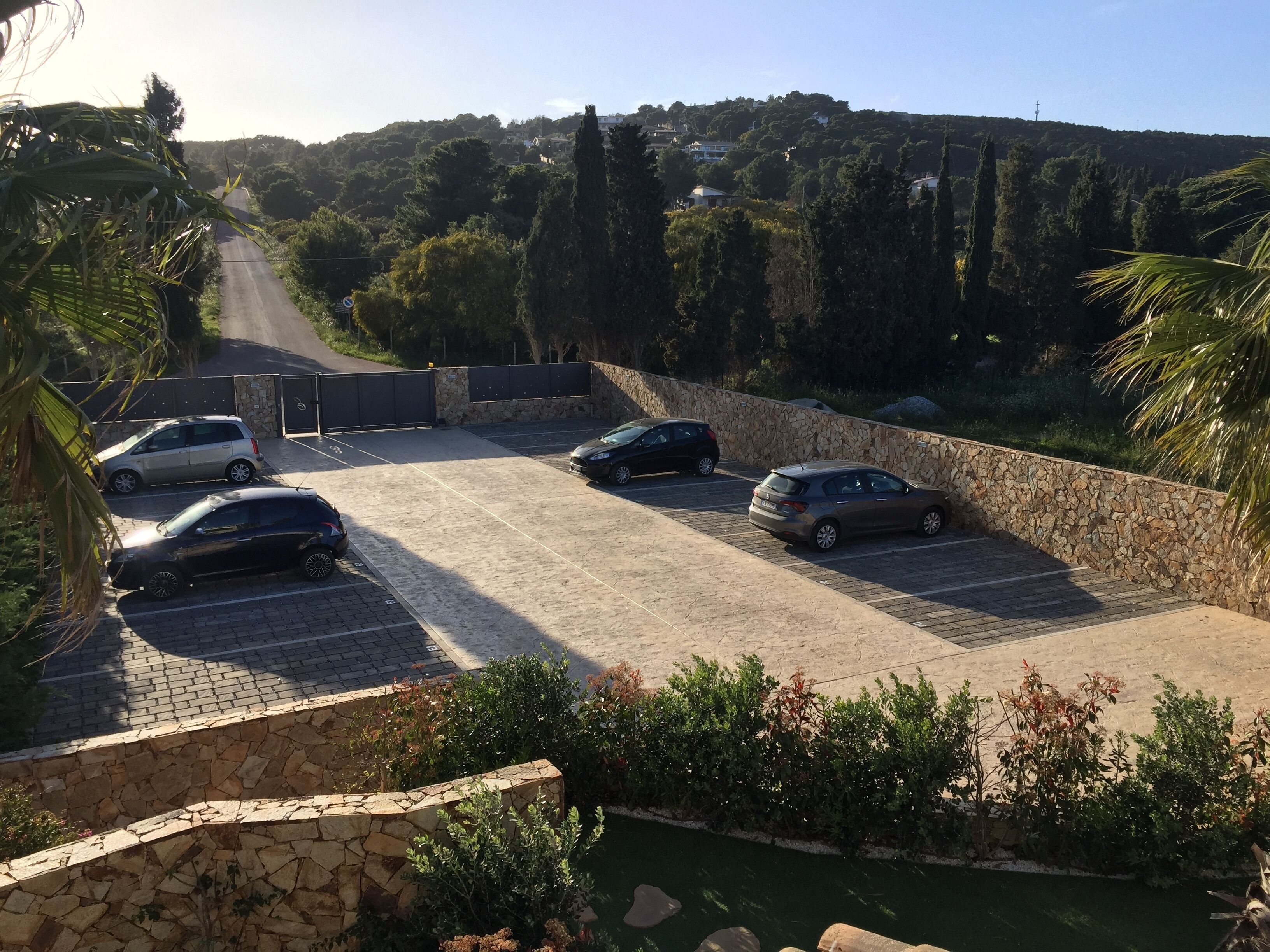 A parking area with several cars, surrounded by stone walls and greenery.