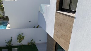 Un patio moderno al aire libre con piscina, zona de estar y pequeños árboles.