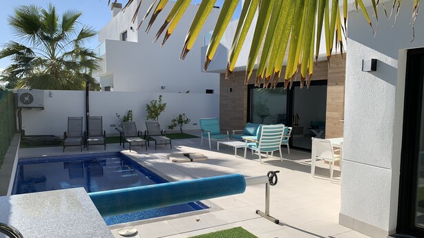 Un área de piscina exterior moderna con piscina rectangular, sillas de descanso y una mesita.