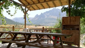 A wooden deck with picnic tables and a wooden cabinet, overlooking a mountainous landscape.