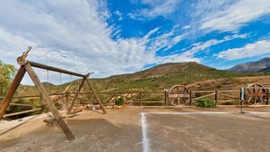 A rustic wooden fence with a swing set and a dirt path leading to a mountainous landscape.