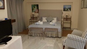 Ein Hotelzimmer mit einem Bett, zwei Nachttischen, einem Sessel, einem Fernseher und Bildern an den Wänden.