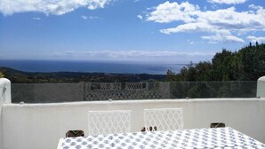 Eine Terrasse mit Tisch und Stühlen, mit Blick auf eine reizvolle Landschaft und den Meerblick sowie hügelige Fernen.