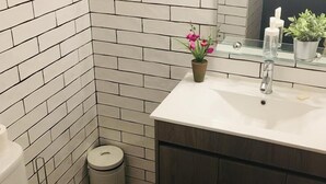 Een badkamer met witte metrotegels, een witte wastafel, een spiegel, een potplant en een toilet.