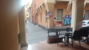 Una calle estrecha con un café a la derecha, que ofrece mesas al aire libre y un mural en la pared.
