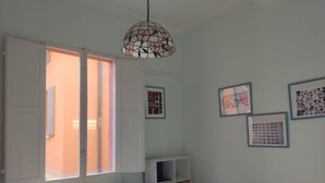 Una habitación con escritorio, silla, ventana abierta, lámpara colgante y estanterías en la pared.