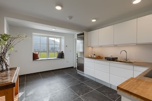 Enjoy a serene view from the large window in this kitchen, featuring white cabinetry and a stainless steel refrigerator.