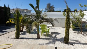 Ein Garten mit einer Palme, einem grünen Stuhl und einer weißen Wand im Hintergrund.