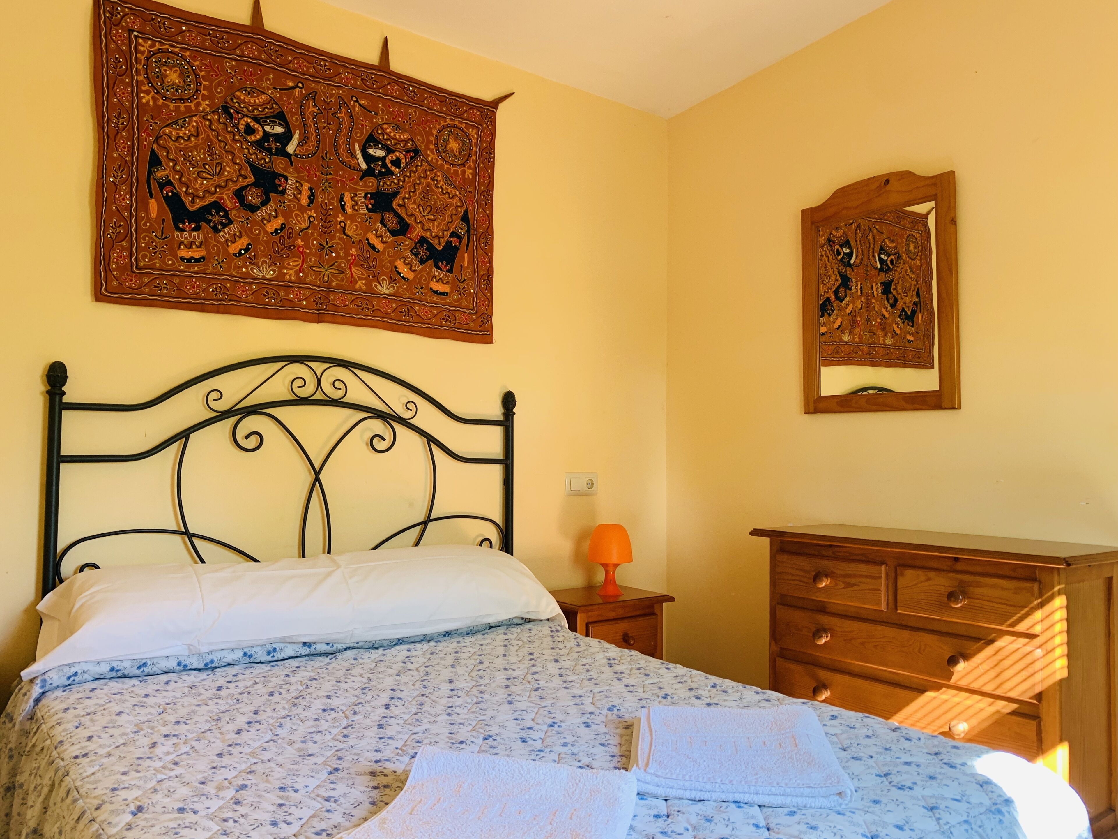 Un dormitorio con una cama, un aparador de madera, una mesita de noche y dos adornos en la pared.