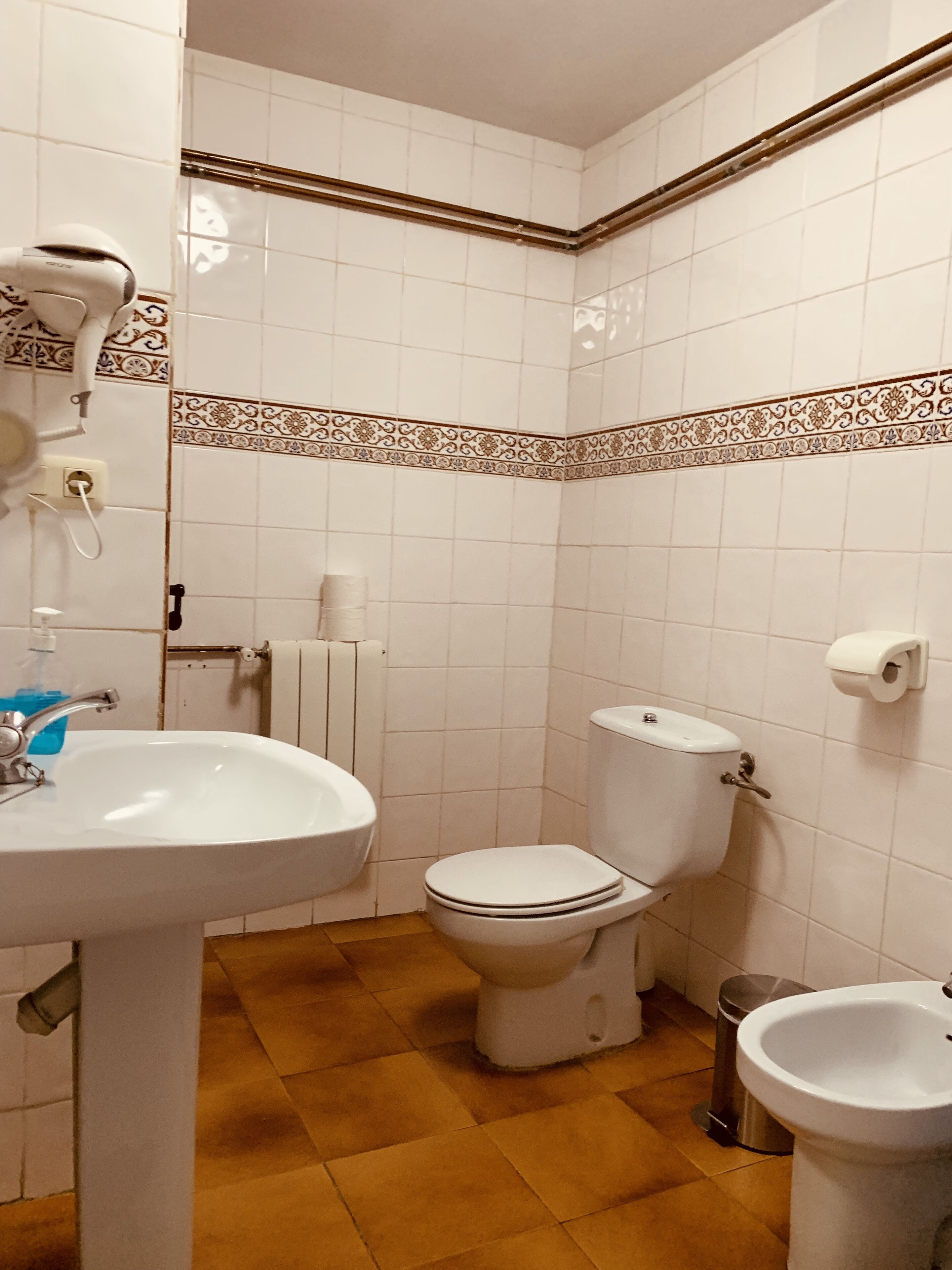 Un baño con lavamanos, inodoro, bidé y un perchero para toallas.