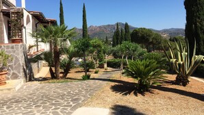 A courtyard with a stone pathway, cypress trees, and a view of distant mountains. - Vista Mare with private pool, large 65,000 square meter garden, sea view, close to the beach.  (Capoliveri)