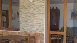A room with a wooden dining table, chairs, a stone wall, and a sliding glass door leading to another room. - Vista Mare with private pool, large 65,000 square meter garden, sea view, close to the beach.  (Capoliveri)