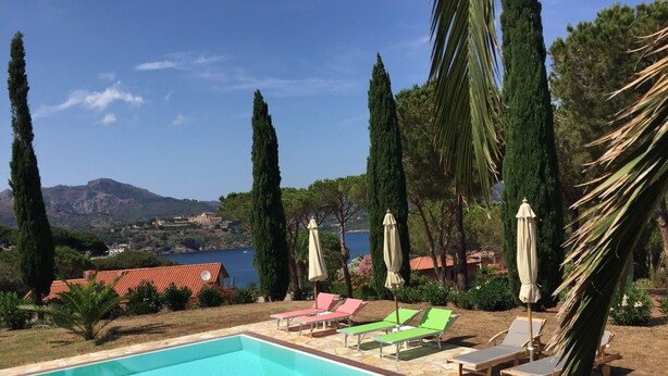 A swimming pool with lounge chairs and umbrellas, surrounded by trees and a view of a mountainous landscape. - Vista Mare with private pool, large 65,000 square meter garden, sea view, close to the beach.  (Capoliveri)