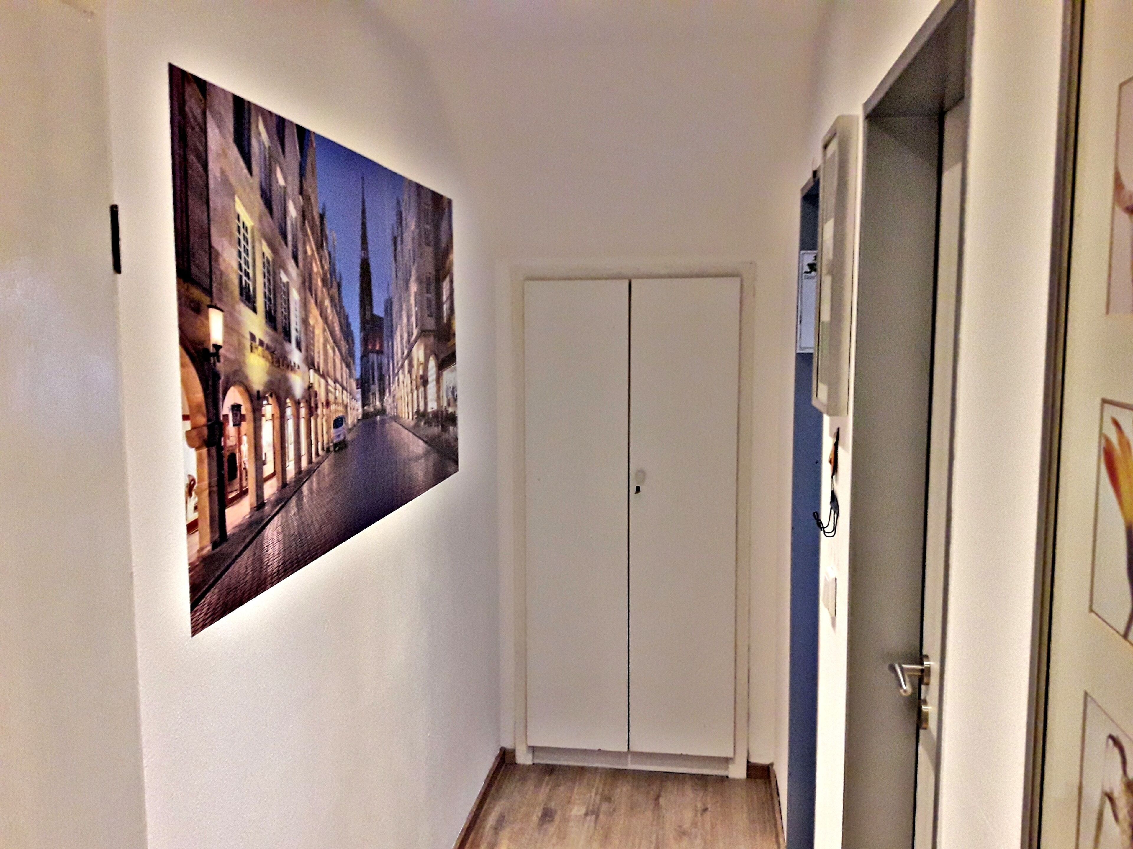 A hallway with a large framed picture of a city street, a white door, and a wooden floor.