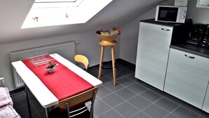 Cocina compacta con comedor, microondas, cafetera y una pequeña mesa con mantel rojo.