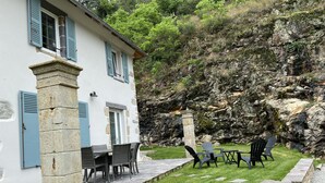 A stone building with a patio area featuring outdoor seating and a view of a rocky hillside. - Comfortable house and neat decoration, view of the Sioule valley. WiFi. (Chateauneuf-les-bains)