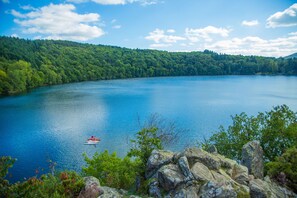 Un lago con un bote, rodeado de bosque denso y terreno rocoso.