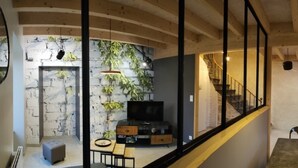 A modern living room with a stone wall, a flat-screen TV, and a dining area with a table and chairs. - Comfortable house and neat decoration, view of the Sioule valley. WiFi. (Chateauneuf-les-bains)