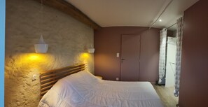 Un dormitorio con cabecera de madera, cama con ropa blanca, dos lámparas fijadas a la pared y una puerta.