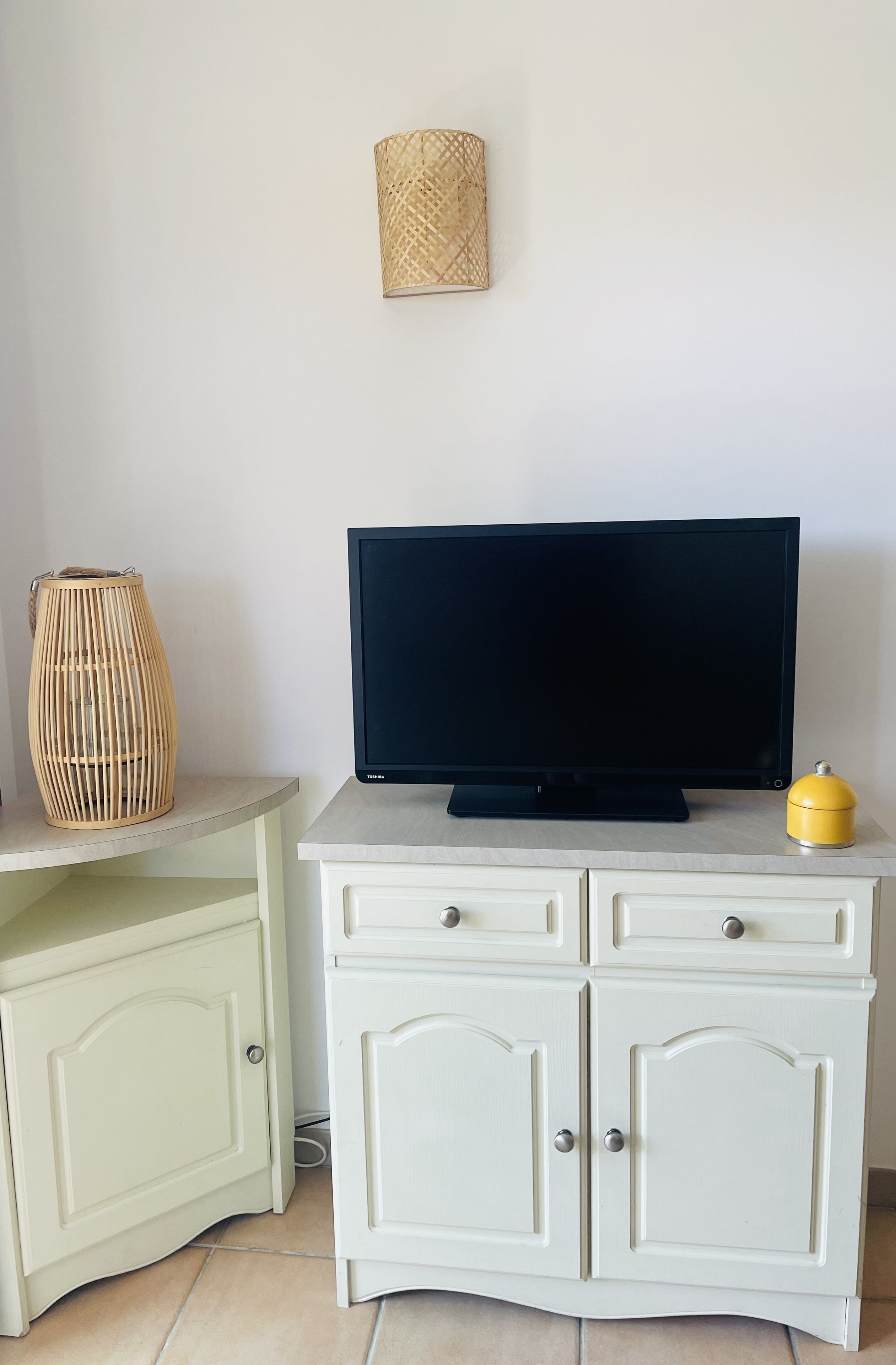 Ein weißes Schranksystem mit Fernseher, einer gewobenen Lampe und einem gelben Gegenstand darauf.