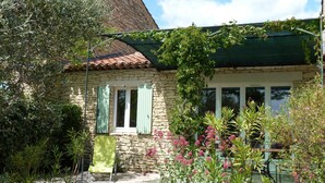 A stone house with a green roof, a small porch with a chair, and a garden with various plants and flowers. - Charming Bastidon with Terrace, Garden, and Pool in Gordes, Luberon  (Gordes)
