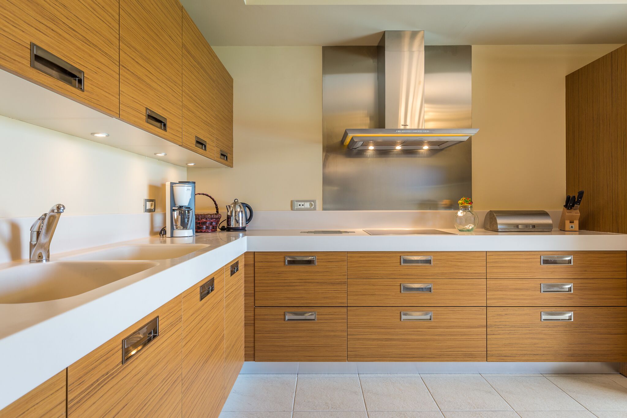 Una cocina moderna con armarios de madera, una campana extractora de acero inoxidable y una encimera blanca.