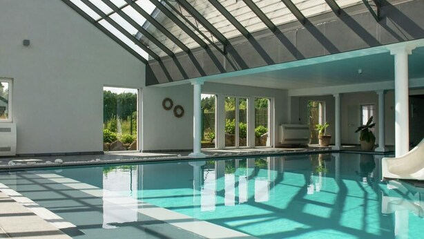 An indoor swimming pool with a glass ceiling, clear water, and a sunlit area with plants and seating. - house with private pool, jacuzzi, sauna, hammam for 4 adults, 2 children (Theux)