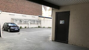 Een parkeerplaats met een zwarte auto, nabij een gebouw met een bakstenen muur en een deur.