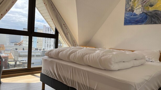 Een slaapkamer met een bed, een groot raam en een schilderij aan de muur.