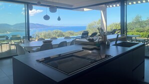 A modern kitchen with a large island, dining area, and a view of the sea. - Villa Lourada architect house, swimming pool, spa 1.5 km from beautiful beaches  (Olmeto)