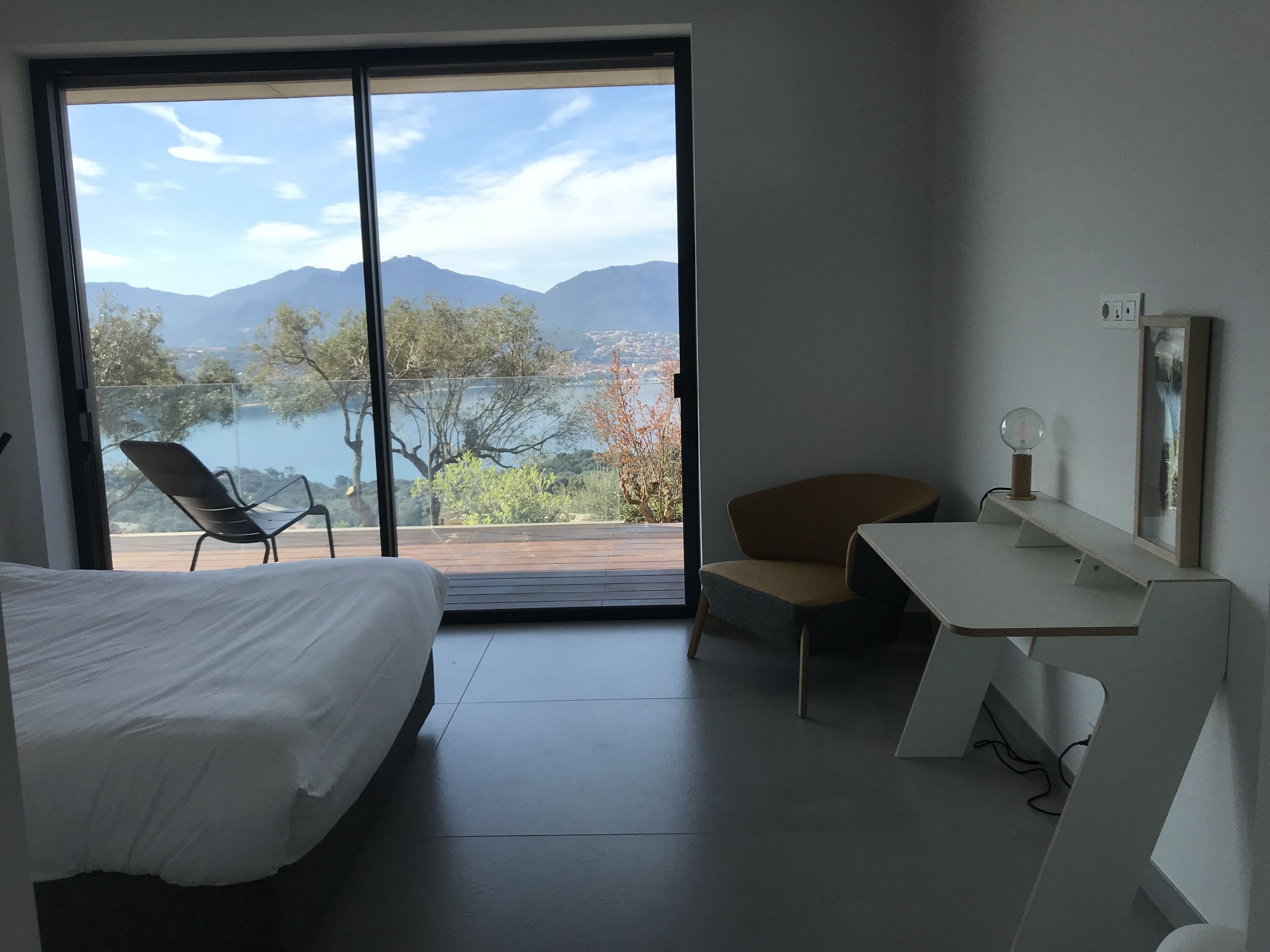 A modern hotel room with a large sliding glass door leading to a balcony with a scenic mountain view.