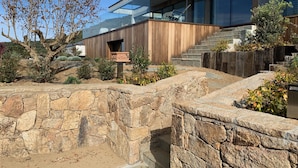 A modern building with a stone retaining wall, wooden steps, and a glass facade. - Villa Lourada architect house, swimming pool, spa 1.5 km from beautiful beaches  (Olmeto)