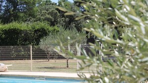A swimming pool with a fence, trees, and a building in the background. - Family farmhouse in Provence on a vineyard with authentic swimming pool (Mondragon)