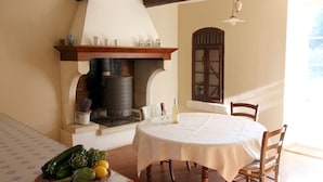 A dining area with a round table, chairs, a fireplace, and a window. - Family farmhouse in Provence on a vineyard with authentic swimming pool (Mondragon)