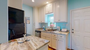 A kitchen with white cabinets, a black refrigerator, a marble countertop, and a window with blinds. - Shared Pool, Walk Path to Beach, Golf Cart Access (Port Aransas)