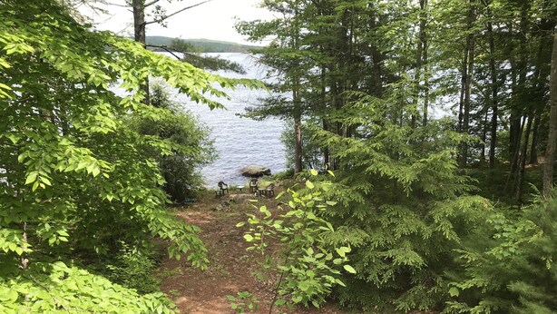 A view from a wooden deck overlooking a lake, with a picnic table and chairs in the foreground. - Luxury Lakefront Living in Lake Sebago Area (Bridgton)