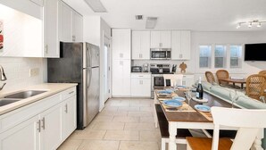 A modern kitchen with white cabinets, stainless steel appliances, and a dining area with a wooden table and chairs.