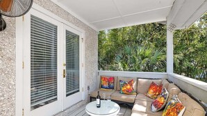 A covered outdoor seating area with a table, cushions, and a bottle of wine.