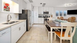 A modern kitchen with white cabinetry, a stainless steel refrigerator, and a dining area with a wooden table and wicker chairs.