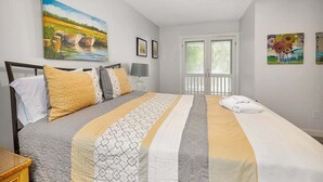 A bedroom with a bed, pillows, a bedside table, a lamp, and artwork on the walls.