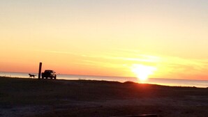 A sunset over a beach with a truck and a dog.