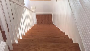 A wooden staircase with white railings leading to a landing. A framed picture hangs on the wall at the landing.