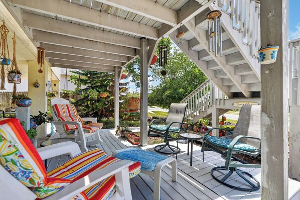 A covered outdoor seating area with multiple chairs and tables, surrounded by potted plants and a wooden deck.